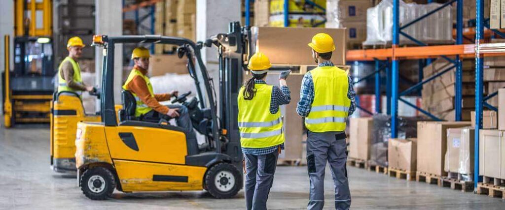 Warehouse workers standing to the side of a forklift discussing fulffilment optimization