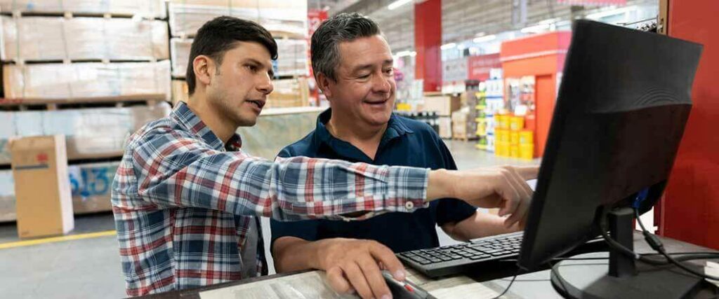 Two warehouse workers examining data on a PC monitor.